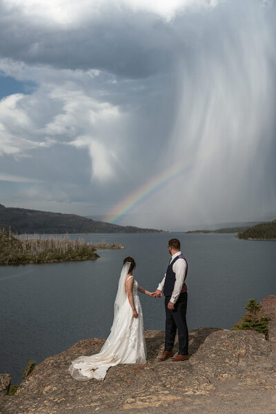 A couple holds hands beneath a star-filled sky reflected on Lake McDonald in Glacier National Park, captured by Sydney Breann Photography during their romantic night elopement.
