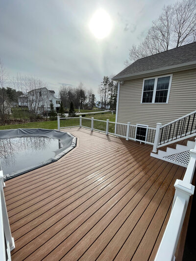 A beautiful dark brown deck with white railings and trellis stairs facing around a pool