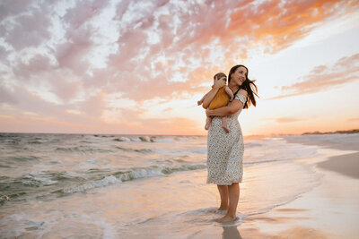 Family Photographer, a mother holds her baby close before a beautiful sunset at sea
