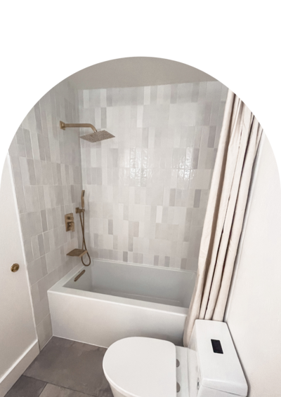 A bathroom remodel with a large white soaking tub, vertical grey and white glossy tiles, and gold hardware.