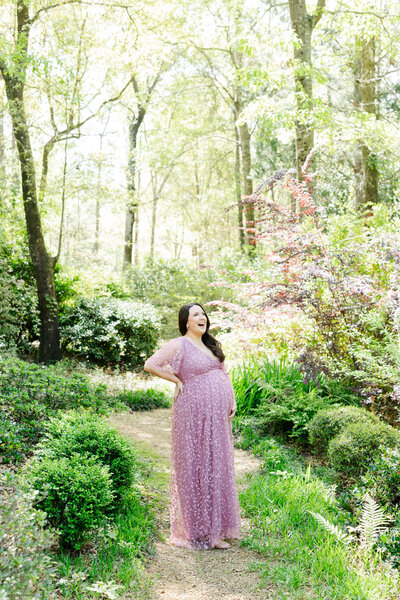 Woman with purple dress on holds her pregnant belly in the middle of the woods for a maternity photography session with Josie Kitch Photography