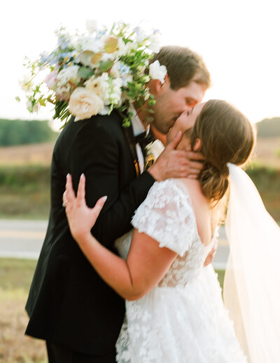 Glowy image of bride kissing groom holding her bouquet with her arm wrapped around him