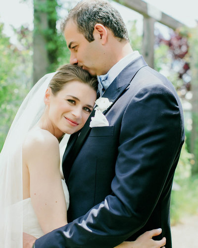 Bride lays head on Grooms chest looking at the camera as he kisses the top of her head
