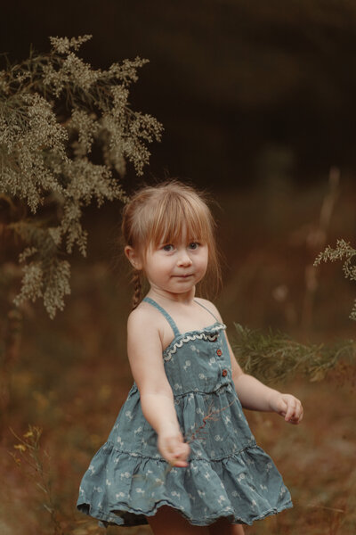 Little girl in denim dress dances with flowers in a field of tall grass by Lawrenceville Child Photographer