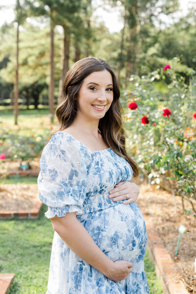 Mother holding pregnant belly smiling at the camera posing in a garden