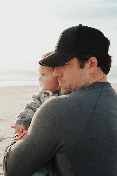 A man on the beach holds a baby in his lap, both enjoying a peaceful moment together on the sandy shore.