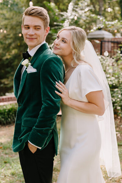 Bride looks at groom in green suit smiling.