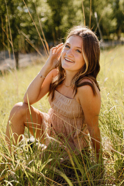 High school girl sitting in a field and smiling at the camera