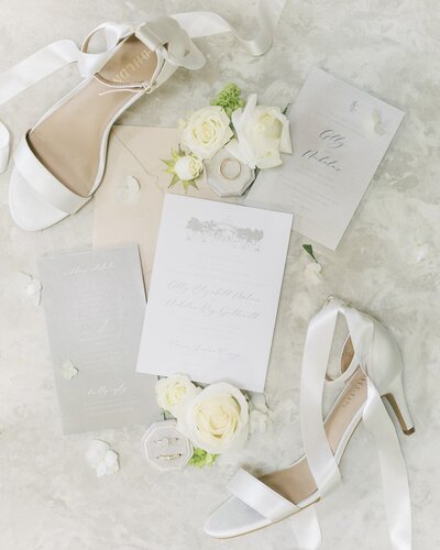 Flatlay with invitation, shoes, vows, and florals