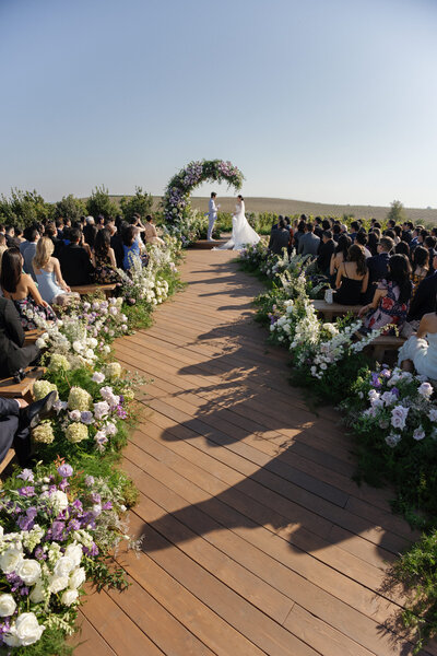 Bride and groom at wedding ceremony altar under large crescent floral arch
