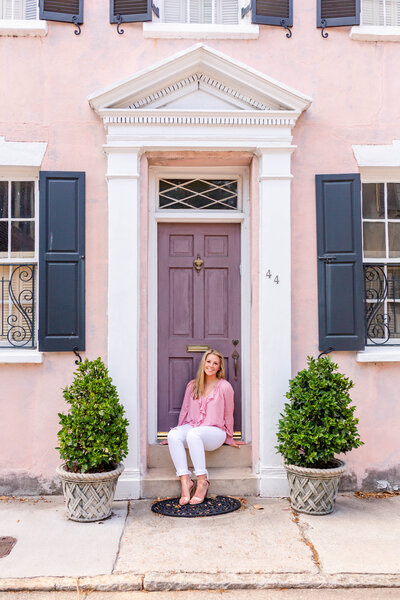 senior girl in pink shirt and white jeans sitting on steps of old house in downtown Charleston