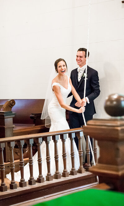 Excited bride and groom ringing a bell at St. David’s Church in Austin, Texas, celebrating their wedding with joy and laughter.
