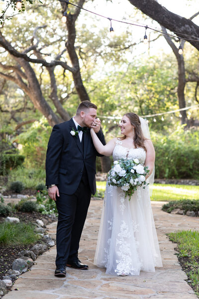 An Austin-based wedding photographer captures a heartfelt moment as a bride and groom share a sweet kiss on a path in a garden.