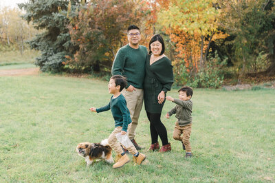 An Edmonton Asian family wearing green and light neutrals having fun with their dog and children.