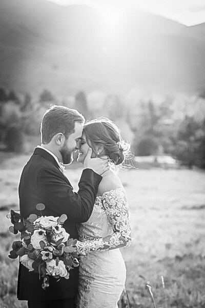 A groom strokes his bride on the cheek as the two stand forehead to forehead at The Manor House at golden hour.