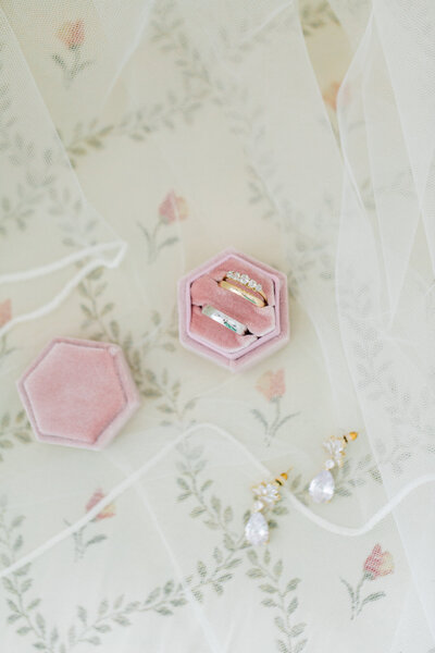 Wedding rings in a pinkk velvet ring box alongside some pearl droplet earrings