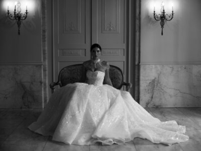 April M Payne Photography captured a bride sitting elegantly on a vintage sofa, wearing a stunning, sparkly ball gown, in a timeless black-and-white portrait with soft lighting highlighting her grace.