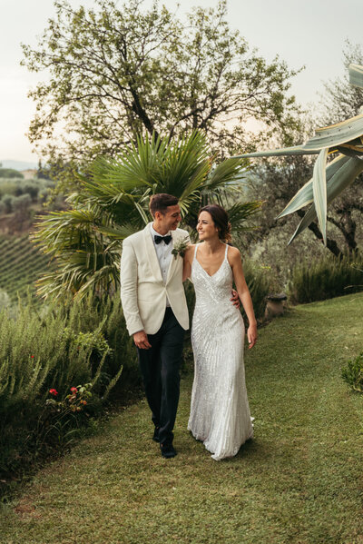 This breathtaking photo captures a newlywed couple walking hand in hand through the lush green hills of Tuscany, Italy. The bride and groom are beaming with happiness and love, and the scenic landscape creates a stunning backdrop for the moment. The image exudes a sense of peace and serenity, and perfectly captures the romantic and enchanting atmosphere of Tuscany