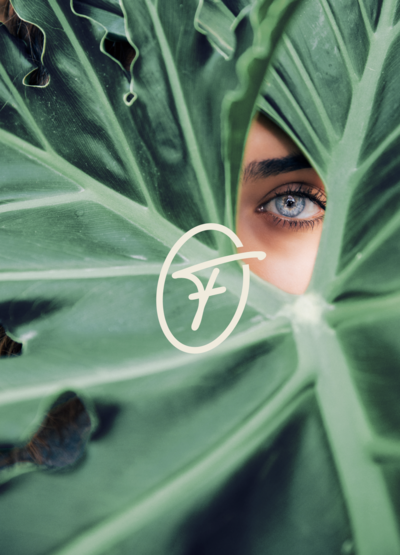 Logo icône French Flow incrusté sur une photo représentant une plante verte à travers laquelle on aperçoit l'oeil bleu d'une femme.