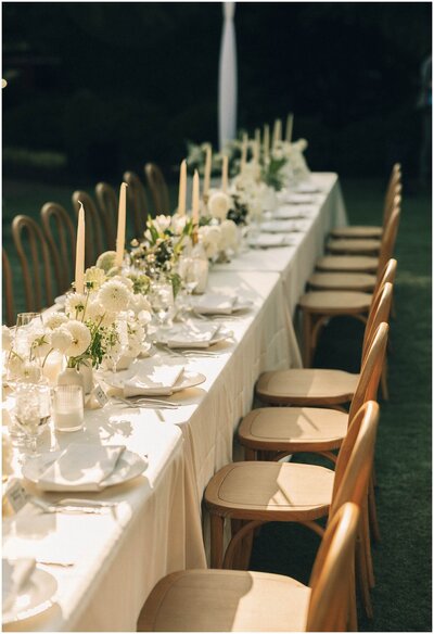 Details looking down a long wedding reception table with white florals outdoors
