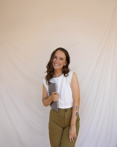 A woman smiling with a stack of graphic design books, a coffee, and a colorful bouquet of flowers.