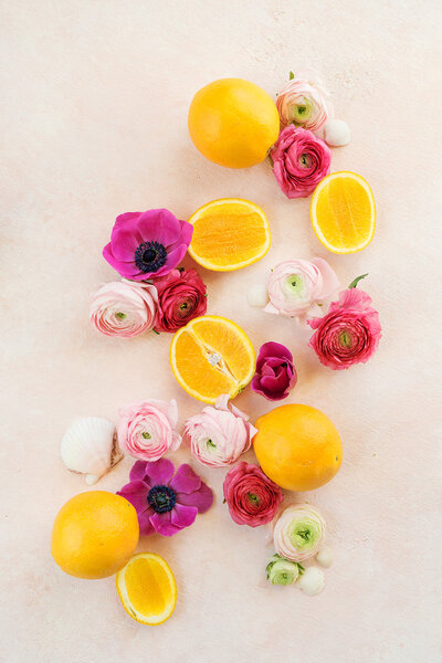 pink flowers and oranges surround an engagement ring sitting inside cut orange on pink mat