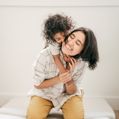 mom smiling while being hugged by toddler child - hypnotherapy based programs for early motherhood 
