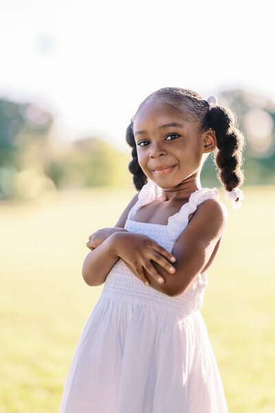 Young girl with pigtails and a white dress crossing her arms