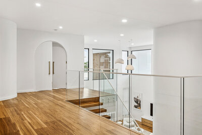 The upstairs hallway in the Marisol home, featuring a glass balustrade, pendant lighting, and a custom arch doorway.