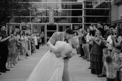 wedding photo of groom dipping his bride to give her a kiss while exiting their venue