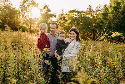Family with little kids laughing together  during candid photo session and having a good time in a beautiful field with golden light in Bath, Ohio.