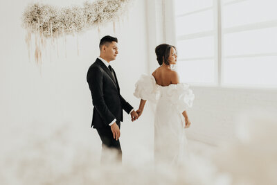 bride and groom holding hands and looking sideways with floral backdrop