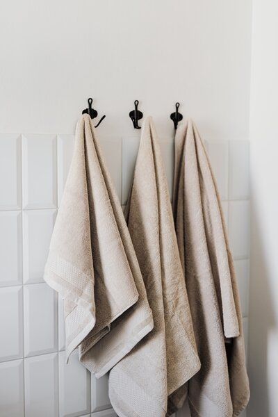 Three soft, neutral-toned towels hang neatly on black hooks, offering a warm, inviting atmosphere and the promise of a spa-like experience