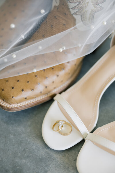 Rings on a pair of heels next to a pair of boots which is partially concealed by a veil.