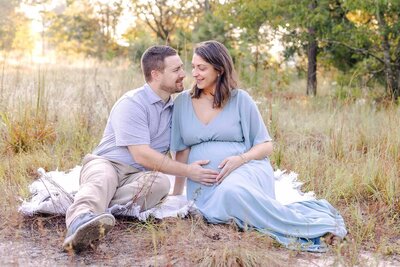 Couple in a field looking at each other while feeling their babies kick in Lexington SC