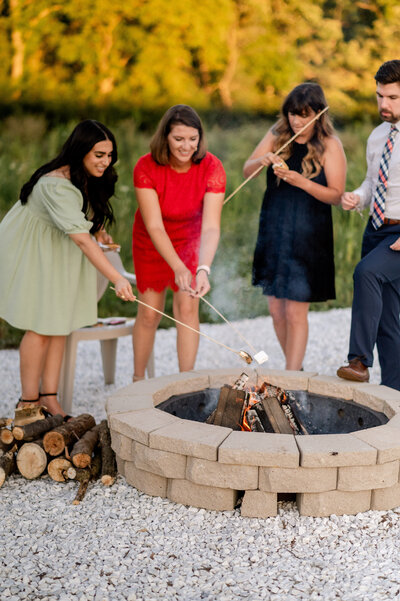 Photo of wedding guests roasting marshmallows around campfire at The Eloise