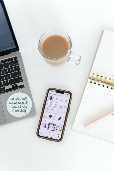 Flatlay of coffee mug with coffee next to an iphone and pink earrings