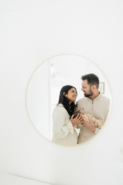 A creative shot of parents with their baby reflected in a mirror, emphasizing the artistry of Cleveland lifestyle newborn photography.