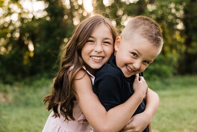 Two smiling children hugging each other outdoors in a delightful family photo captured in Pittsburgh.