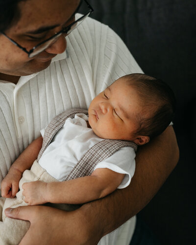 Dad holding newborn son in arms and gazing down adoringly.