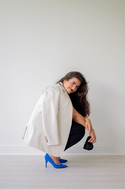 Hiba, creative behind Moments by Hiba, posing with a camera and bright blue heels during Raleigh branding photography session.