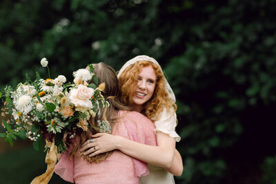 Bride Peyton Curry embraces her best friend with joy after saying "I do" at her intimate backyard wedding in Richmond, Virginia. Captured by a film wedding photographer in a candid, documentary-style moment.