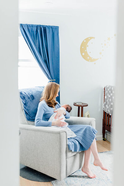 View through doorway of a mom holding her newborn in a rocking chair in his nursery