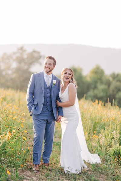 Bride and groom smile in a field of flowers in the piedmont region of Virginia.