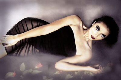 A beautiful woman in a black lingerie dress is surrounded by red roses in dry ice.