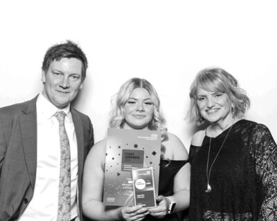 Black & white photo of a group with a lady in the middle, holding an Awards Ceremony for the NHS, during a corporate event at the Cheltenham Race Course