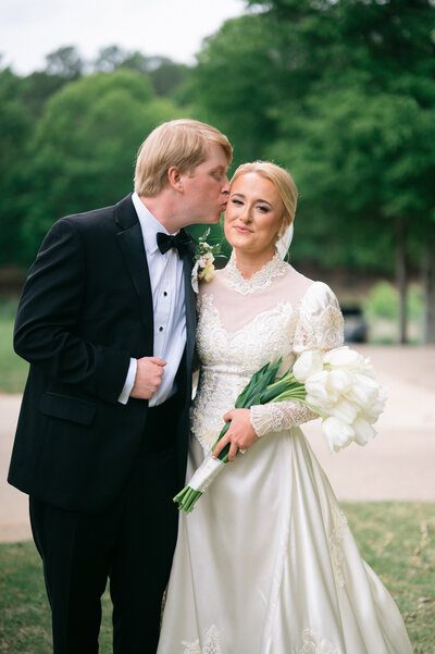 Groom leaning in and kissing bride on cheek while she is holding a bouquet of tulips