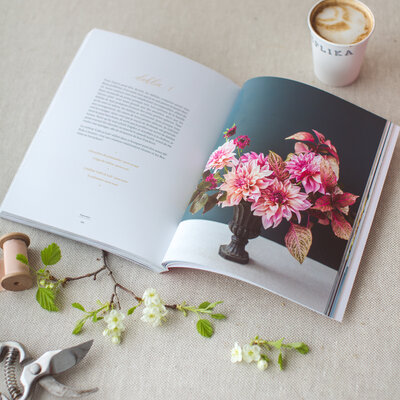 A book on flower arranging sits on a table, open to a photo of a pink bouquet.