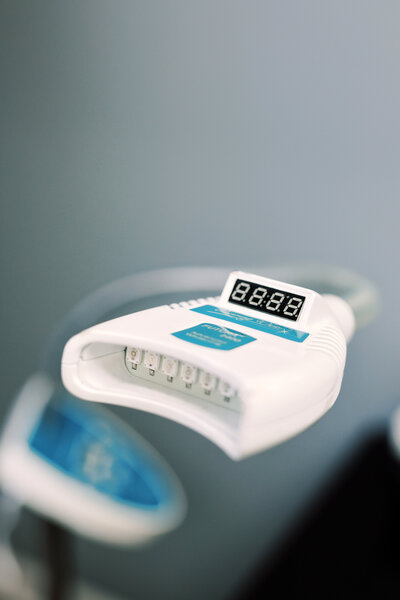 UV teeth whitening tool with a sleek design, featuring a small handheld device with a light emitting from the tip. The device is placed near a set of teeth, indicating the whitening treatment process. The tool is compact, with a modern and ergonomic look, and is designed to help brighten teeth with ultraviolet light.
