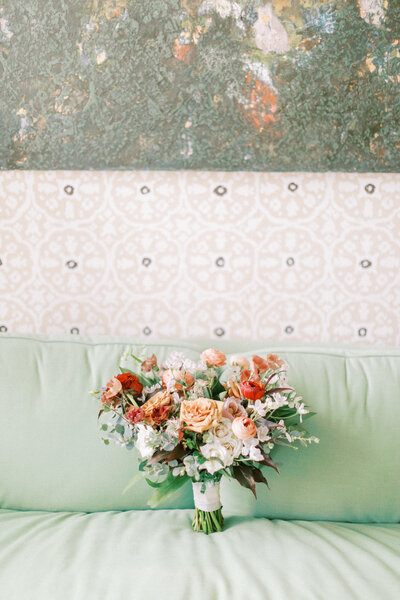 a bride's bouquet in orange tones sitting upright on a green couch.